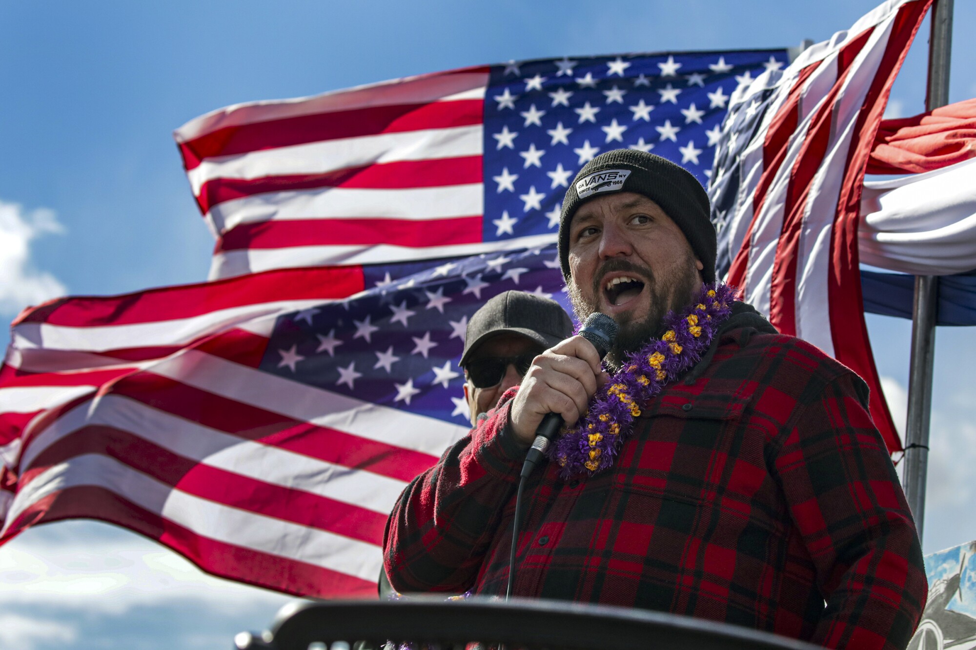 Trucker Brian Brase speaks at a rally, with American flags behind him