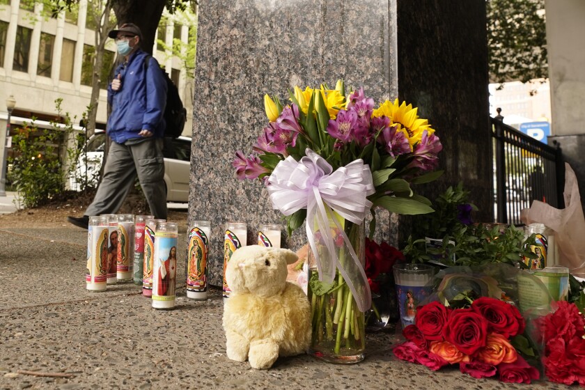 A person passes a memorial of flowers, candles and a stuffed animal.