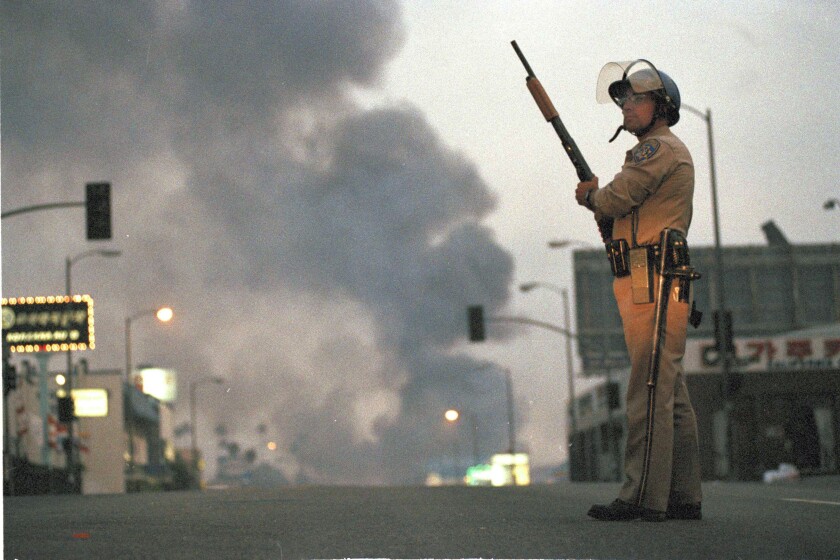 A California Highway Patrol officer on a street, with smoke in the background.