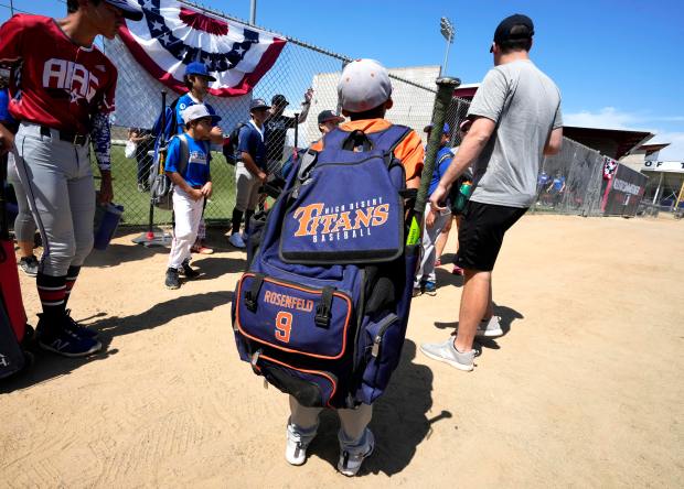 A young baseball player carrying a baseball backpack listens to...