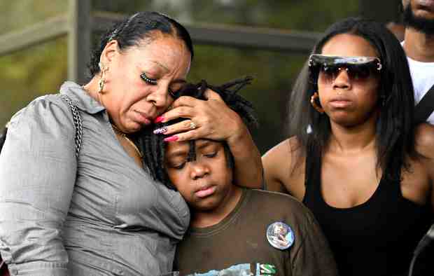 Tamika King, mother of Robert “Rob” Adams, left, comforts younger...